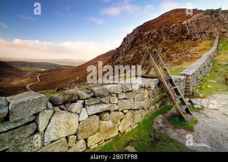 Trauernde Mauer mit Leiter auf der Hare-Lücke, die das schöne Tal mit blauem Himmel und weißen Wolken beaufsichtigt. Mourne Mountains Range in Nordirland Stockfoto