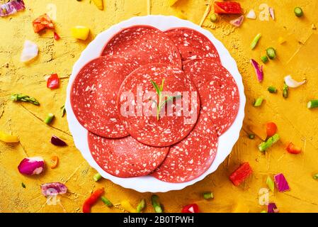 Hohe Winkelansicht einiger Scheiben von veggie Salami in einem Teller, auf einer goldfarbenen strukturierten Oberfläche Stockfoto