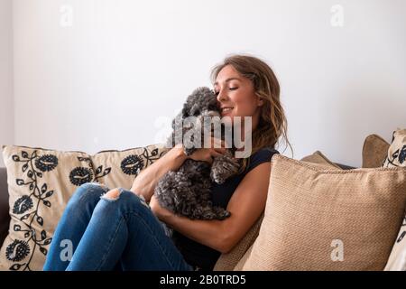 Junge Frau, die auf dem Sofa sitzt und Kakapfuh-Welpe kuschelt Stockfoto