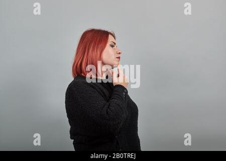 Junge Rotkopf-Fette-Dame im schwarzen Pullover denkt, berührt Kinn mit der Hand Stockfoto