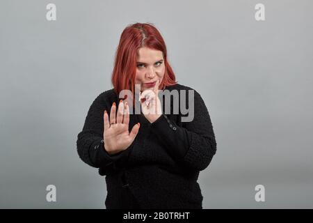 Geheimnisvolle Frau hält mit Handfläche an, hält Stoppschild, hält Zeigefinger nahe dem Gesicht Stockfoto