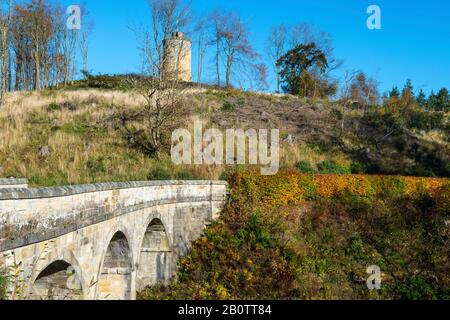 Steinbogenbrücke an der Haupteinfahrt mit Knight's Law Tower im Hintergrund, Penicuik Estate, Midlothian, Schottland, Großbritannien Stockfoto