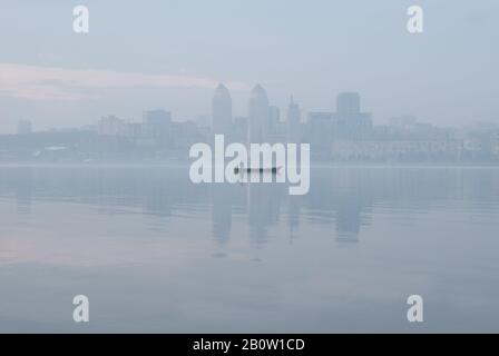 Fischerboot auf dem Dnjepr Fluss in der Ukraine vor dem Hintergrund der Stadt Dnipro im Morgennebel. Dnipro ist mit abou die viertgrößte Stadt der Ukraine Stockfoto