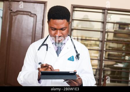 Der männliche Arzt, der an einer Tablette arbeitet und die Uniform der Ärzte in einem Krankenhaus oder einer Arztpraxis trägt. Stockfoto