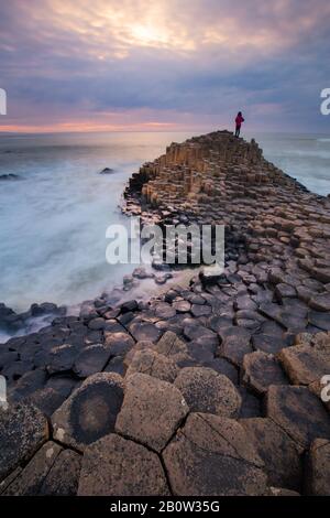 Silhouette von Menschen, die bei Sonnenuntergang in Nordirland auf den Giant Causeway Felsen stehen Stockfoto