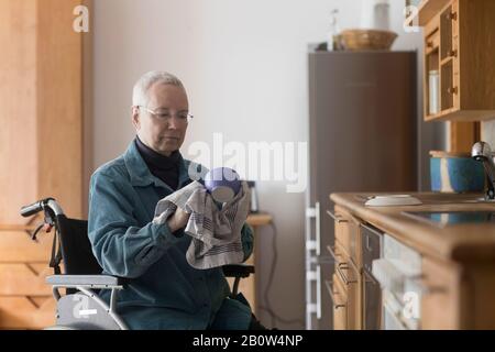Seniorin sitzt im Rollstuhl in ihrer Küche, dryng nach oben. Stockfoto