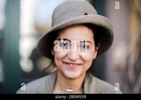 Porträt einer lächelnden jungen Frau mit braunem Haar, mit Hut und Blick auf die Kamera. Stockfoto