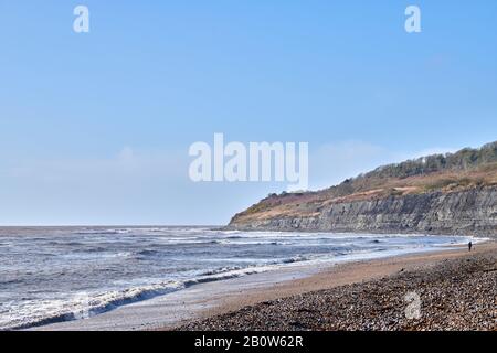 Wellen vom Ärmelkanal brechen am Schindelstrand der Lyme Bay, Lyme Regis, Dorset, England mit den Klippen der Heritage (Jurassic) Coast, A. Stockfoto