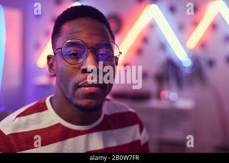 Portrait des afrikanischen jungen Mannes in Brillen, die beim Besuch der Party auf die Kamera blicken Stockfoto