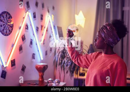 Afrikanische junge Frau, die gegenüber der Wand steht und Darts spielt, die sie auf der Party lustig hat Stockfoto