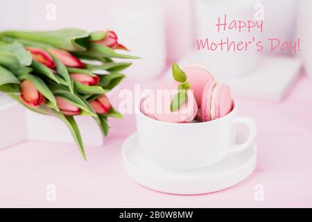 Happy Mother's Day Konzept. Beschriftung, Text, Wörter. Rosafarbene Makronen und Frühlings-Tulpen auf pinkfarbenem Hintergrund Stockfoto