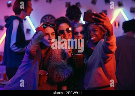 Eine Gruppe glücklicher Mädchen, die selfie auf dem Handy stehen und machen, während sie auf der Disco-Party Spaß haben Stockfoto