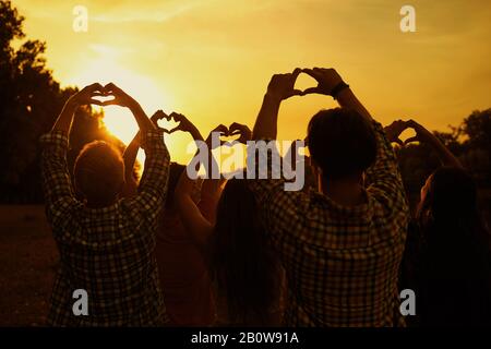 Ein Herz, das von den Händen einer Gruppe von Menschen bei Sonnenuntergang gebildet wird Stockfoto