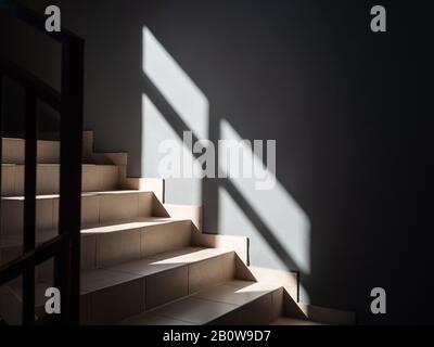 Fotos von hellen Stufen und einer grauen Wand, die von der Sonne aus dem Fenster und mit dem fallenden Schatten beleuchtet werden Stockfoto