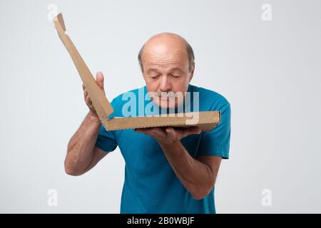 Der Senior hält eine offene Schachtel mit heißer Pizza und schaut auf das Essen. Hungriger Mann mit leckerer Pizza in den Händen. Fast-Food-Konzept. Stockfoto