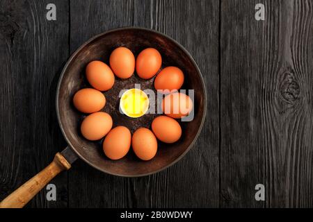 Zehn braune Hühnereier in einem alten gusseisernen Geschickel blicken in der Mitte auf ein zerbrochenes Ei mit einem hellen Eigelb. Stockfoto