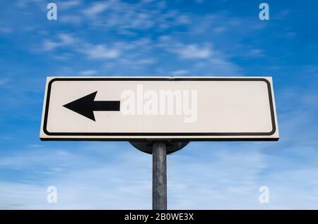 Leeres weißes, nach links gerichtetes Pfeilzeichen mit Kopie auf blau. Weißes Straßenschild mit Pfeil am blauen Himmel mit Wolken Hintergrund. Nach links zeigendes Richtungszeichen Stockfoto