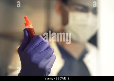 Schließung einer Blutprobe, die von medizinischem Laborpersonal im Hintergrund gehalten wird Stockfoto