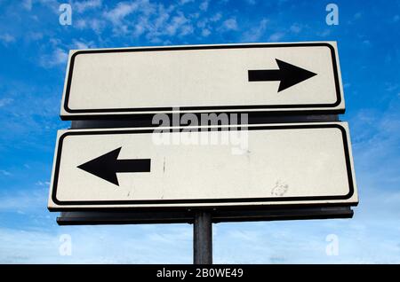 Wegkreuzung Schild, Zwei Pfeile auf blauem Himmel Hintergrund. Doppeltes, leeres Straßenschild mit Kopierbereich. Zwei Pfeile auf einem Pfosten, die in Richtung zeigen Stockfoto