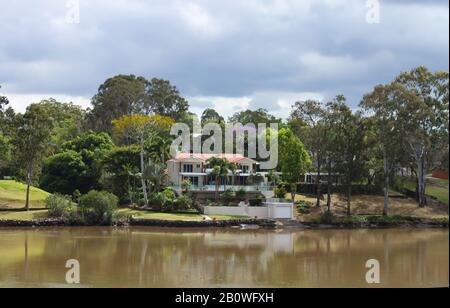 Haus am Fluss in Queensland Australien mit Palmen und hohen Säumenbäumen unter einem stürmischen Himmel im Frühling Stockfoto