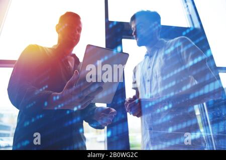 Hintergrundkonzept mit der Silhouette von Geschäftsleuten, die auf das Tablet blicken. Doppelte Belichtung und Lichteffekte Stockfoto