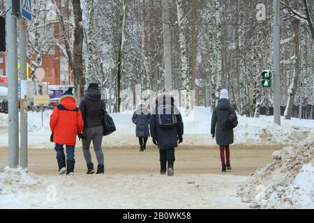 Eine Gruppe von Menschen überqueren die Straße an einem Fußgängerübergang zum grünen Schild einer Ampel vor dem Hintergrund der Winterstadtlandschaft. Stock-Foto mit leerem Platz für Text und Design. Stockfoto