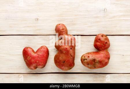 Hässliche Kartoffel in Herzform und Buchstabenform auf weißem Holzhintergrund. Konzept für Gemüse- oder Lebensmittelabfälle. Draufsicht, Nahaufnahme. Stockfoto