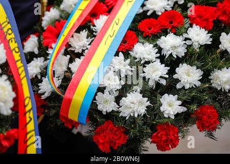 Flache Schärfentiefe (selektiver Fokus) Bild mit roten Gerbera und weißen Chrysanthemumblumen auf einem Trauerkranz mit der rumänischen Fahne auf der Rippe Stockfoto