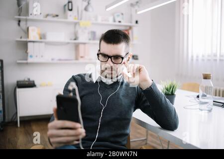 Büro-Mitarbeiter verwenden Telefon und hören Musik im Büro. Der Mensch hört Musik, während er im Arbeitsalltag Routine macht. Stockfoto