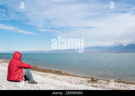 Einsamer Mann, der auf dem Seeufer sitzt und die Natur bewundert. Unerkennbare Person, Wanderlust Stockfoto