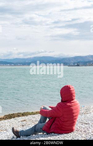 Einsamer Mann, der auf dem Seeufer sitzt und die Natur bewundert. Unerkennbare Person, Wanderlust Stockfoto