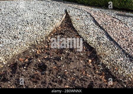 Metalleinkantung, die Schmutz und verschiedene Schotterfarben in einem Park voneinander trennt Stockfoto