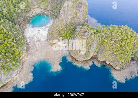 Zerklüftete Kalksteininseln ragen aus der heiteren Seescape in Raja Ampat, Indonesien auf. Diese tropische Region wird als Herz des Korallendreiecks bezeichnet. Stockfoto