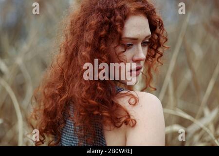 Frau mit langen roten Haaren steht im Schilf, Porträt Stockfoto