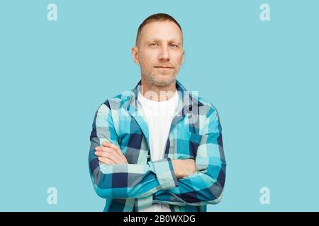 Bärtiger Mann mit gekreuzten Armen und weißem T-Shirt und blauem kariertem Hemd auf blauem Hintergrund. Stockfoto