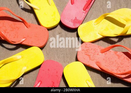 Kreis von Flip-Flops in hellen, sonnigen Farben am glatten Sandstrand Stockfoto