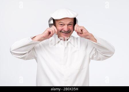 Chefkoch, der seine Ohren mit Kochpfannen über weißem Hintergrund bedeckt Stockfoto