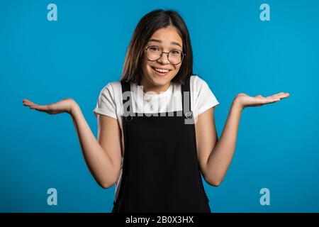 Junge asiatische Unsichere Mädchen in Overalls zuckt ihre Arme, Geste von Ich weiß nicht, Pflege, kann nichts helfen. Stockfoto