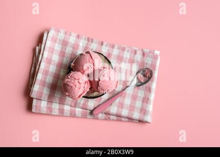 Himbeereis in einer Glasschale auf Serviette, auf pinkfarbenem, nahtlosem Hintergrund. Blick auf das Eis der Beeren. Hausgemachte rote Eiscreme. Sommerdessert. Stockfoto
