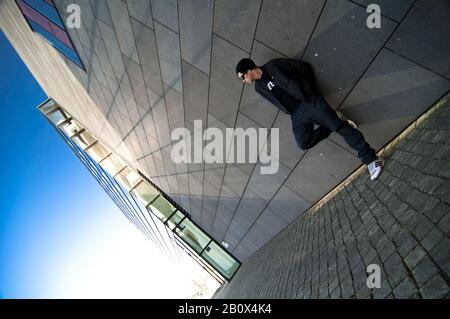 Junger Mann in legerer Kleidung steht vor Hauswand, Stockfoto