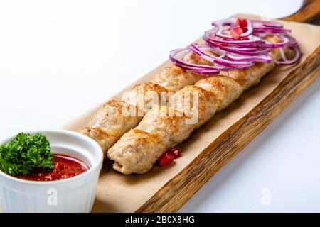 Lula-Kebab von Huhn mit Zwiebeln und heißer roter Soße. Lula wird auf einem Holzteller serviert. Weißer Hintergrund. Stockfoto