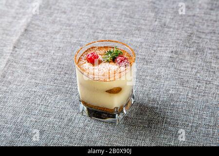 Panna Cotta Dessert aus transparentem Glas, oben mit Kirschen und Minze dekoriert, ein Glas auf grauer Leinwand. Stockfoto
