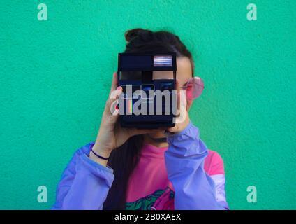 Junge lateinerin, die ein Instanenbild mit farbenfrohem Hintergrund aufgenommen hat. Stockfoto