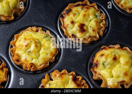 Mit Feta-Käsemischung gefüllte Backbecher aus Filo in einer Backform aus Cupcake. Stockfoto