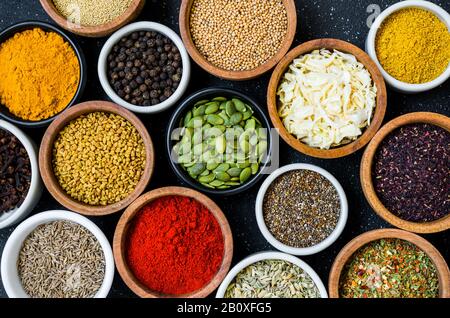 Verschiedene bunte Gewürze, Kräuter und Samen auf schwarzem Steingrund. Stockfoto