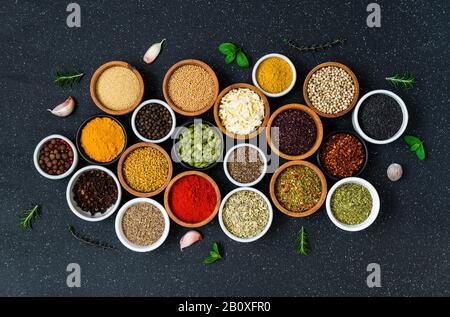 Verschiedene bunte Gewürze, Kräuter und Samen auf schwarzem Steingrund. Stockfoto