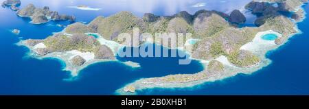 Zerklüftete Kalksteininseln ragen aus der heiteren Seescape in Raja Ampat, Indonesien auf. Diese tropische Region wird als Herz des Korallendreiecks bezeichnet. Stockfoto