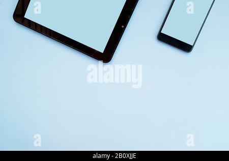 Schwarzes Tablet und Smartphone auf hellblauem Hintergrund. Flaches Lay. Draufsicht. Kopierbereich Stockfoto