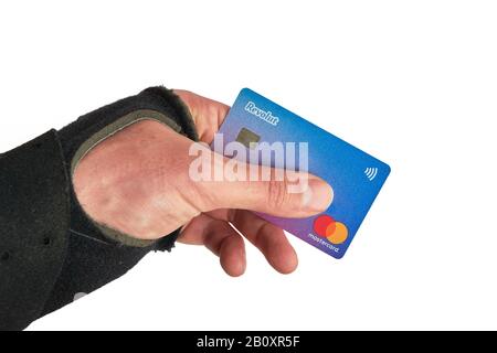 Bukarest, Rumänien - 13. April 2019: Revolut-Master-Karte zwischen den Fingern einer Hand, die eine Handgelenkspange trägt, nach einer Skiverletzung. Stockfoto