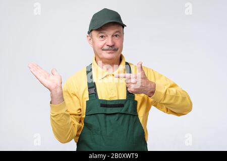 Lächelnder leitender Arbeiter, der die Kamera ansieht und mit dem Zeigefinger zur Seite zeigt. Studio gedreht Stockfoto